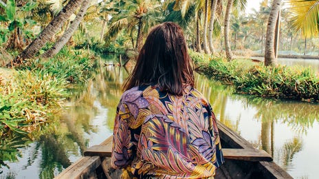 Woman sitting on a wooden canoe navigating a tropical river surrounded by palm trees, an immersive way to learn Malaysian through travel and culture.