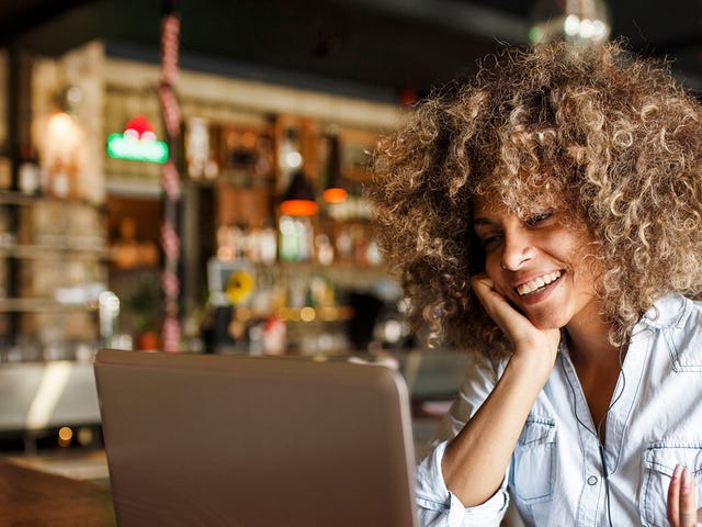 Smiling woman attending online Spanish classes for adults from a cozy café using her laptop
